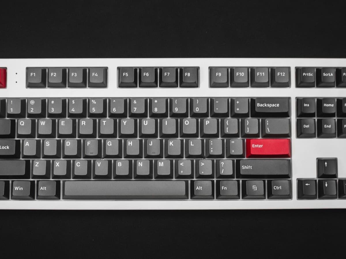A full-size mechanical keyboard with grey keycaps and red accent keys on a dark surface