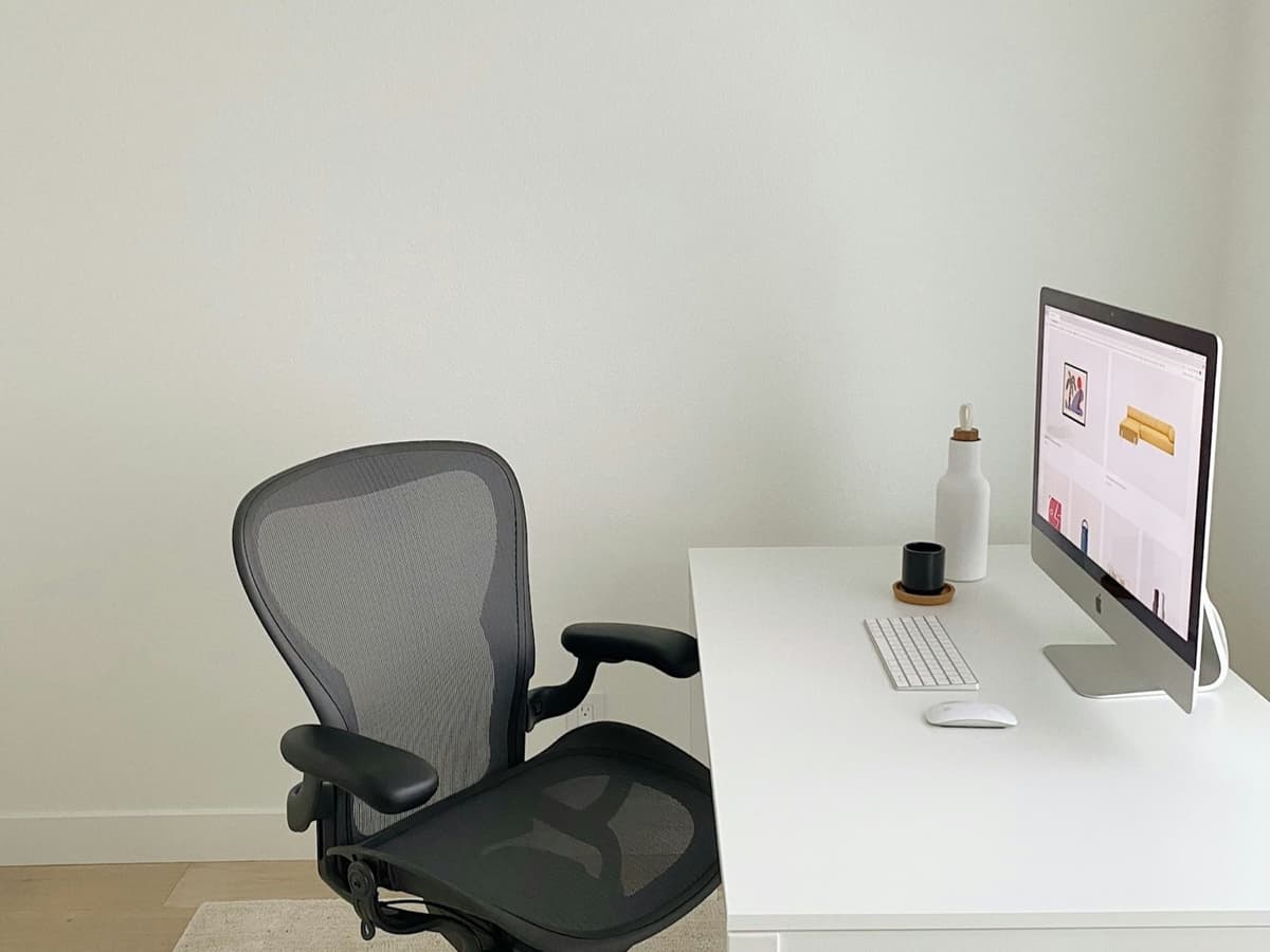 A black mesh office chair beside a white desk in a plain home office
