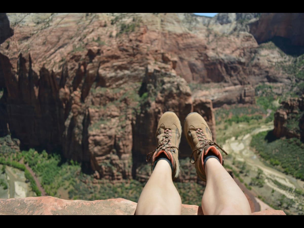 A hiker in brown boots resting on a clifftop above a canyon