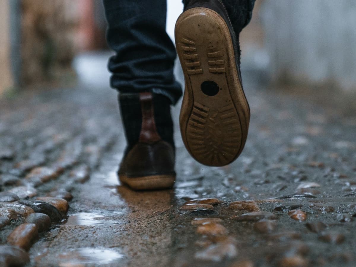 A person walking along a wet cobbled street in leather shoes