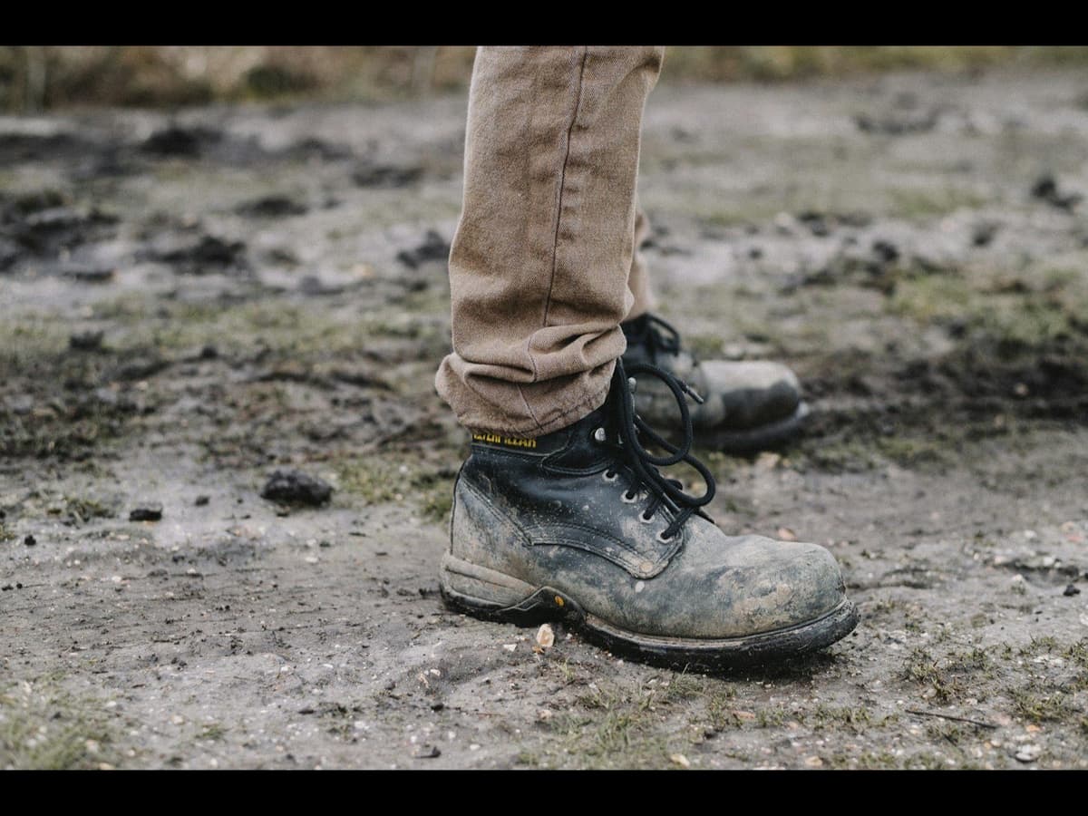 A worker in muddy safety-toe work boots standing on a wet jobsite