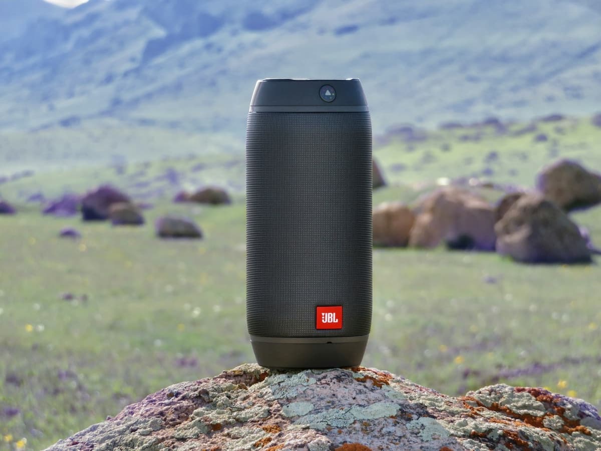 A cylindrical portable Bluetooth speaker on a rock in a mountain meadow