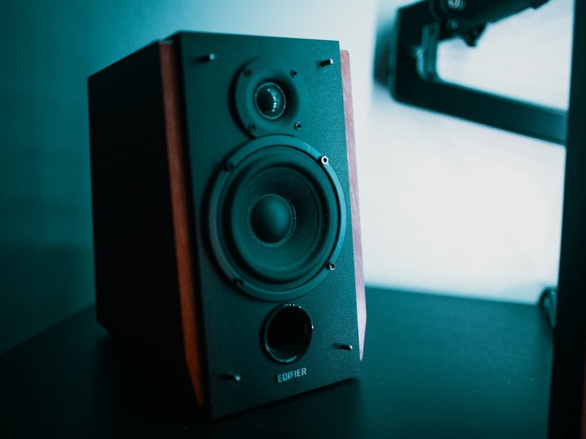 A wooden hi-fi bookshelf speaker with visible tweeter and woofer on a desk