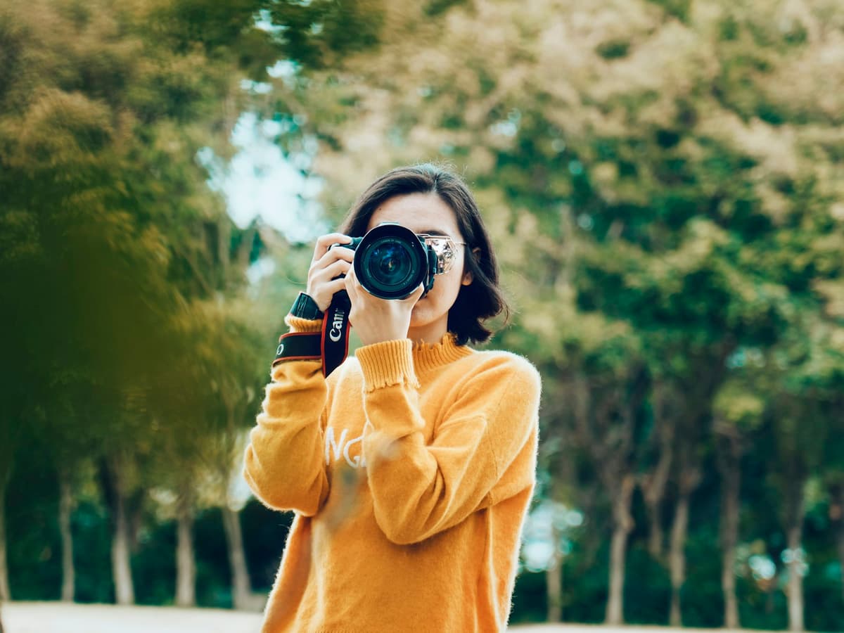 A person raising a camera to their eye to take a photograph outdoors