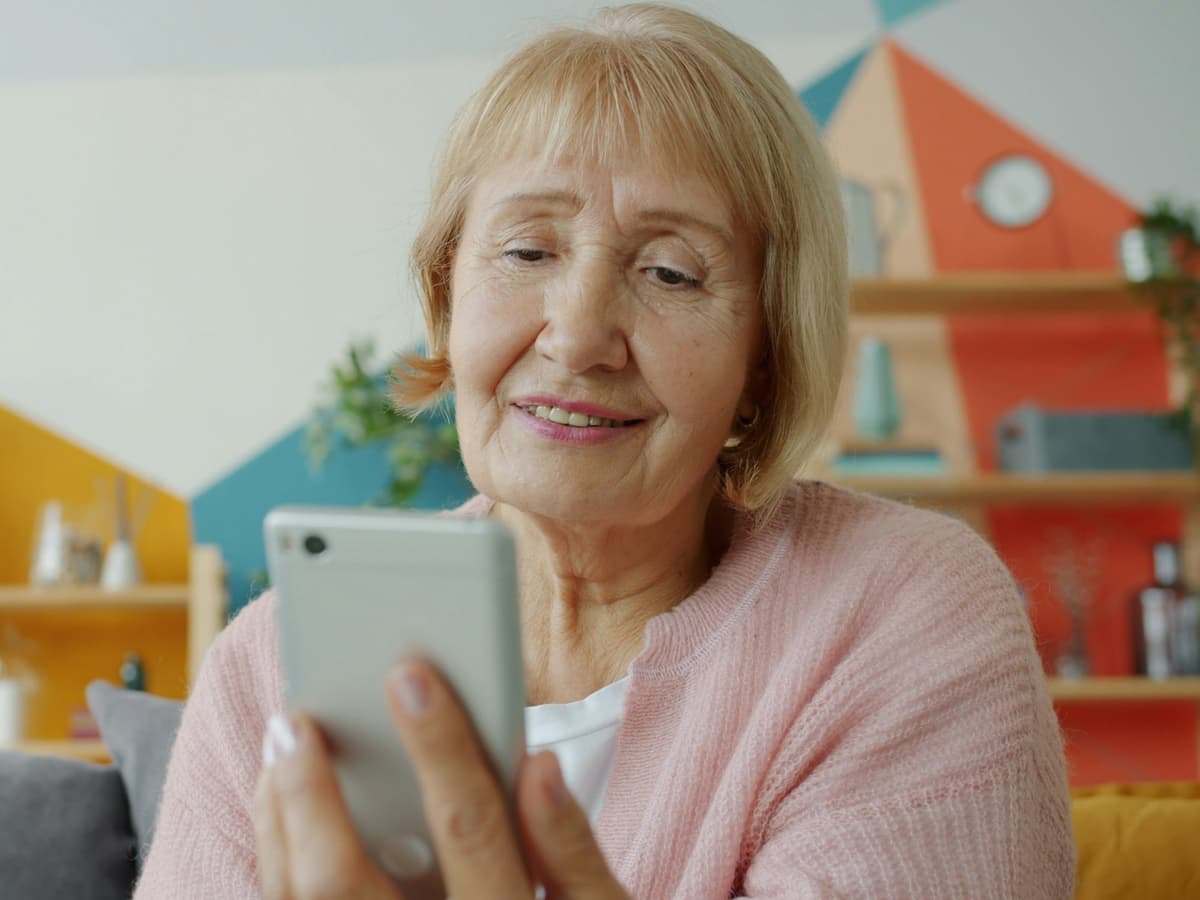 An older woman smiling while using a smartphone at home
