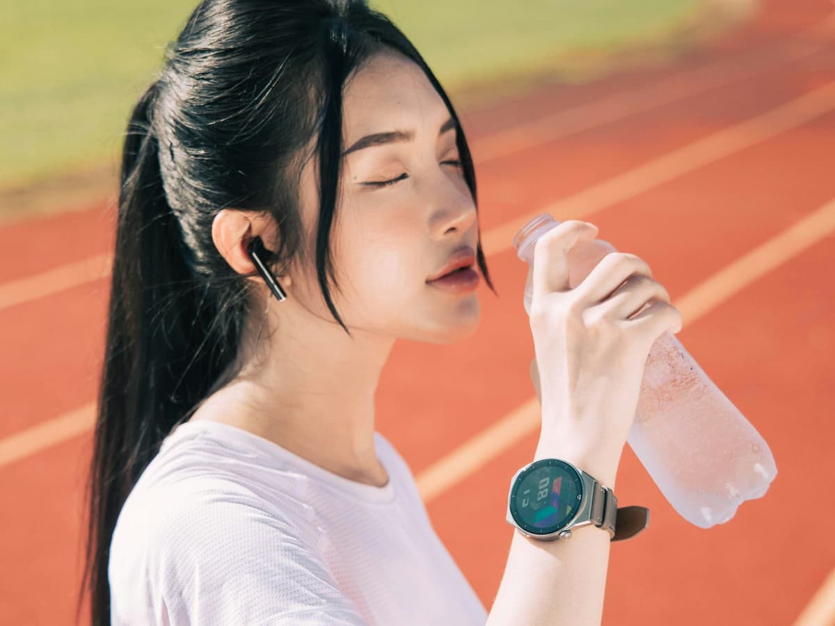 A runner wearing wireless earbuds pausing for water on an athletics track