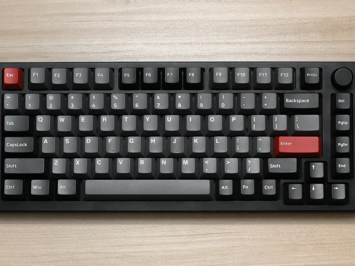 A compact tenkeyless mechanical keyboard with a control knob on a wooden desk