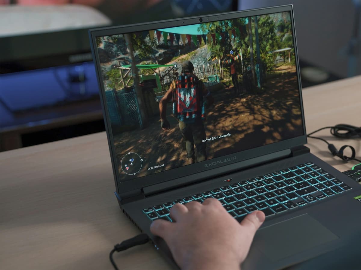 Hands on the backlit keyboard of a gaming laptop running a game