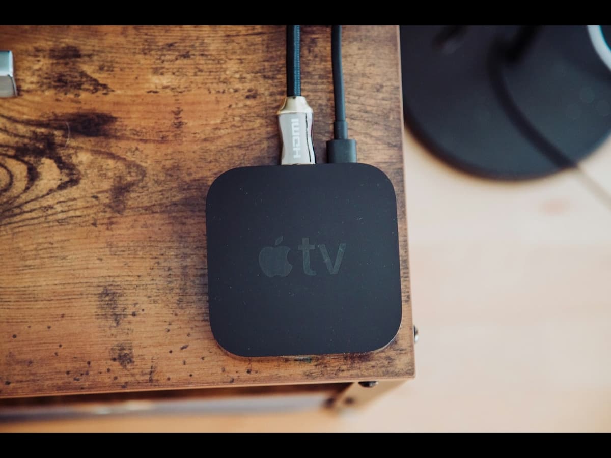 An Apple TV media box connected by HDMI cable, sitting on a wooden media unit