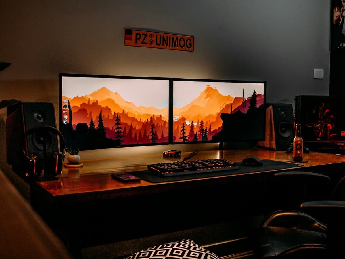 Two monitors side by side on a wooden desk sharing one mountain wallpaper, with a mechanical keyboard in front