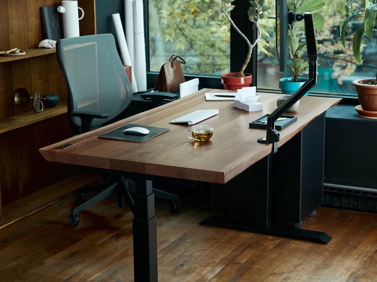 A height-adjustable standing desk with a wood top and black motorised legs in a home office